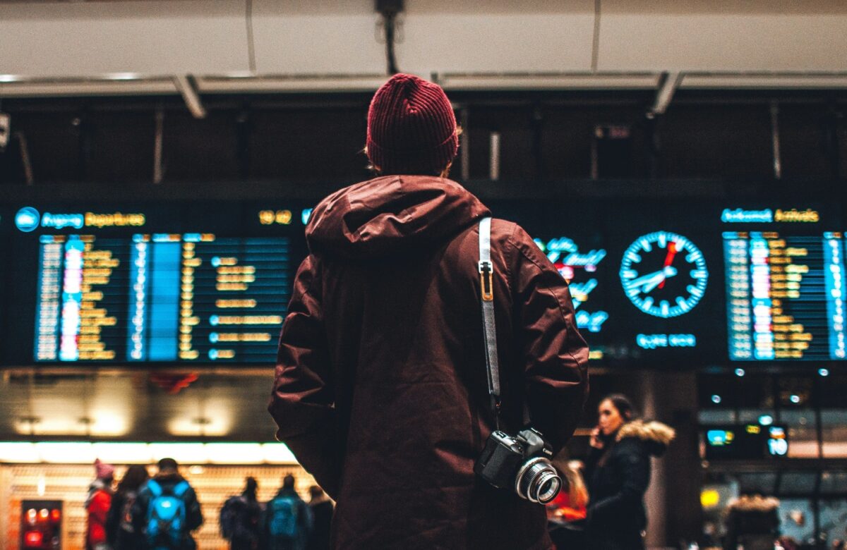 Traveler checking flight schedules at airport, representing budget travel program benefits