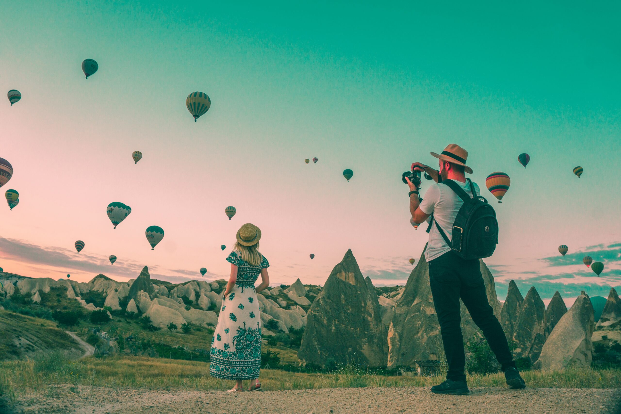 Hot air balloons floating over Cappadocia landscape with travelers watching sunrise